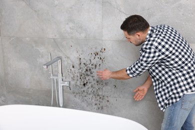 Man looking at affected with mold wall in bathroom