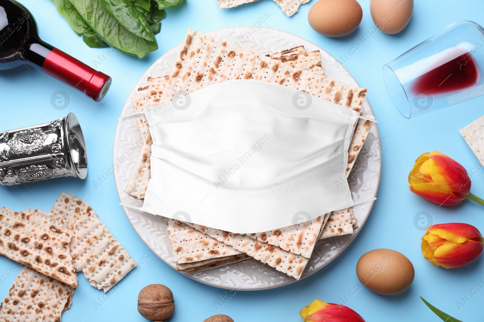 Image of Coronavirus pandemic. Flat lay composition with symbolic Pesach (Passover Seder) items and protective face mask on light blue background