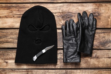 Black knitted balaclava, gloves and knife on wooden table, flat lay