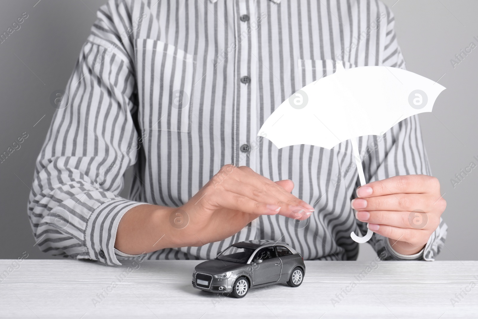 Photo of Insurance agent covering toy car with paper cutout umbrella and hand at table, closeup