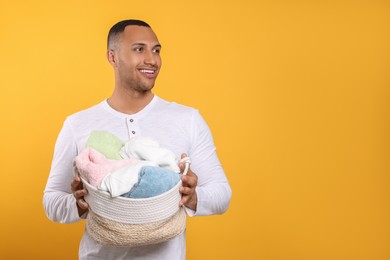 Photo of Happy man with basket full of laundry on orange background. Space for text