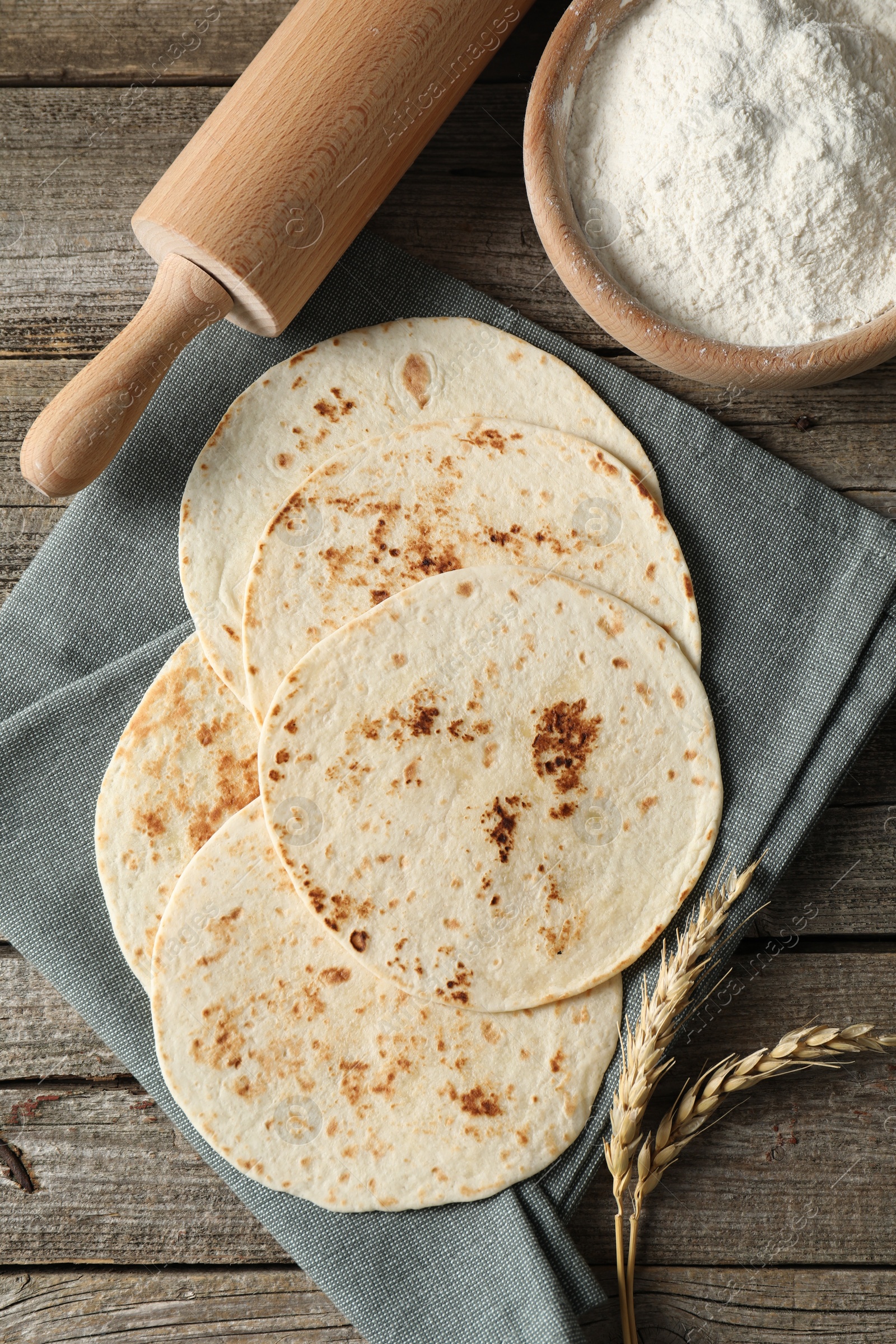 Photo of Tasty homemade tortillas, flour, rolling pin and spikes on wooden table, top view