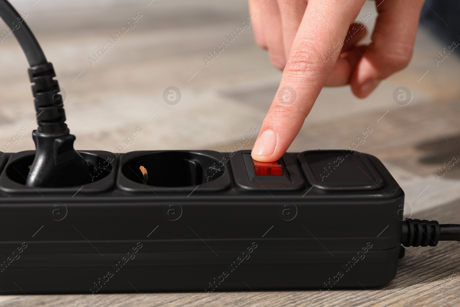 Photo of Man pressing power button of extension board on floor, closeup