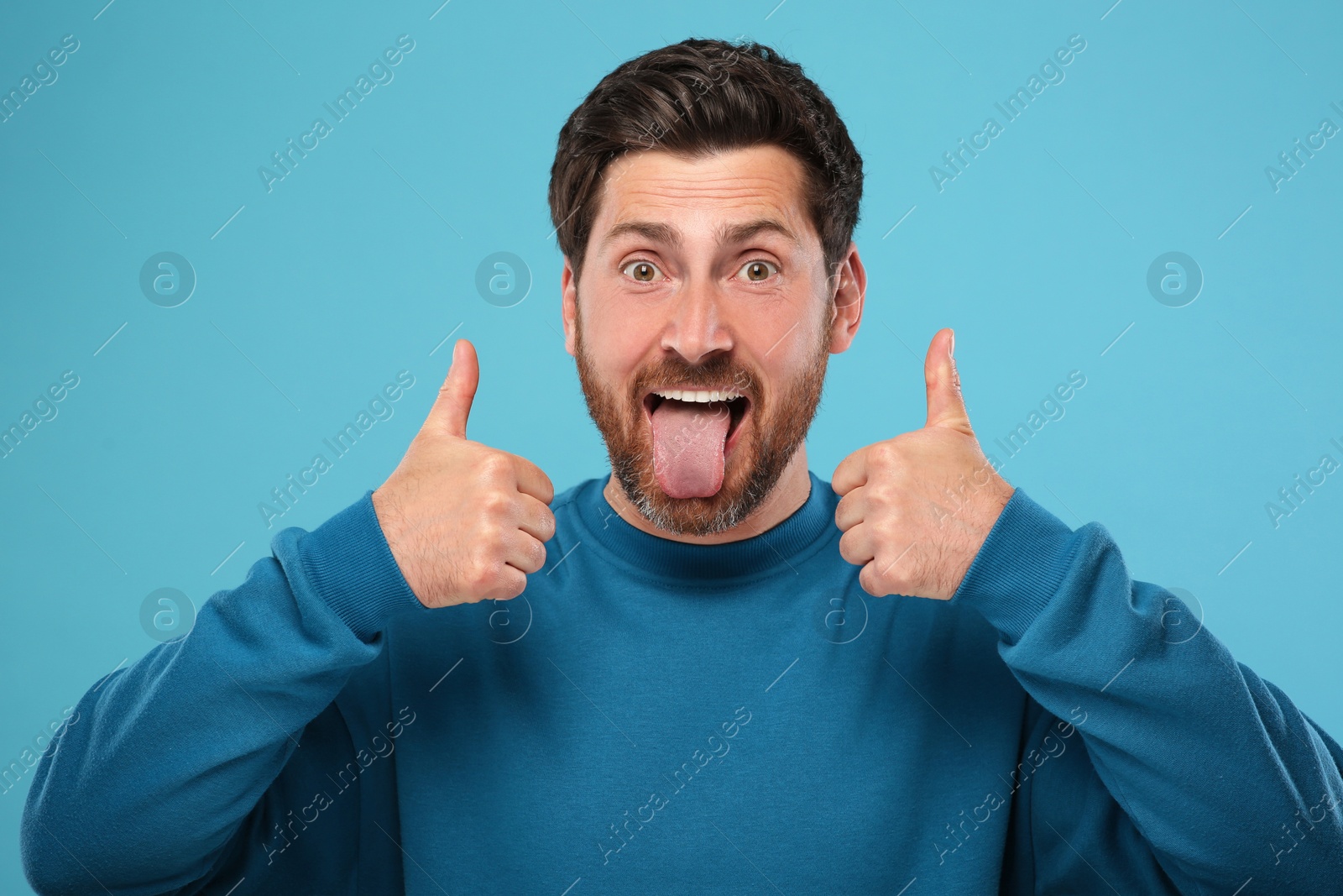 Photo of Man showing his tongue and thumbs up on light blue background