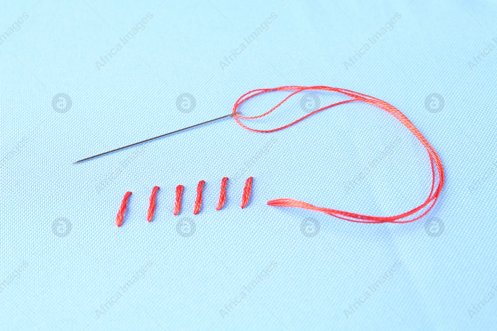 Photo of Sewing needle with thread and stitches on light blue cloth, top view