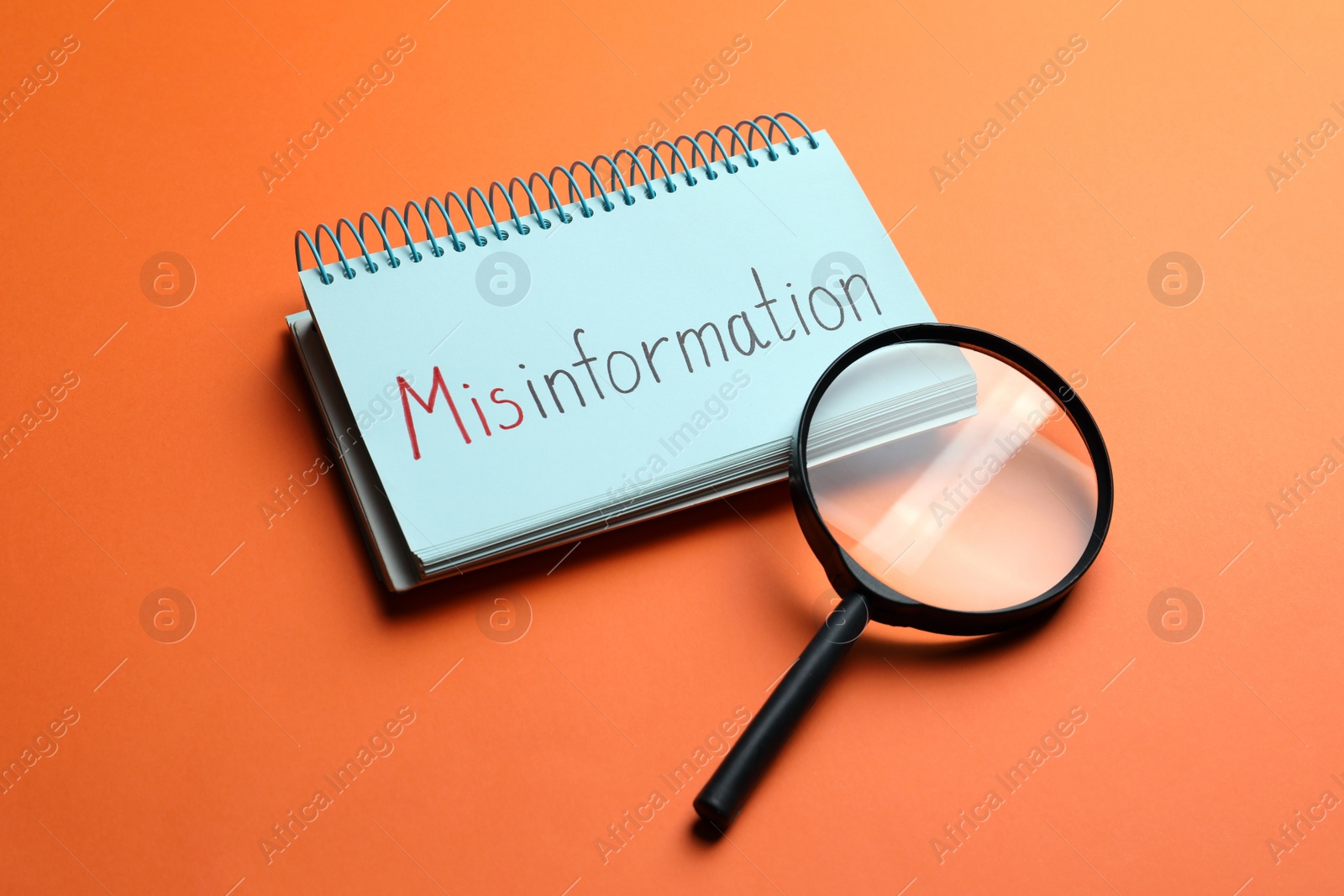 Photo of Notebook with word MISINFORMATION and magnifying glass on orange background