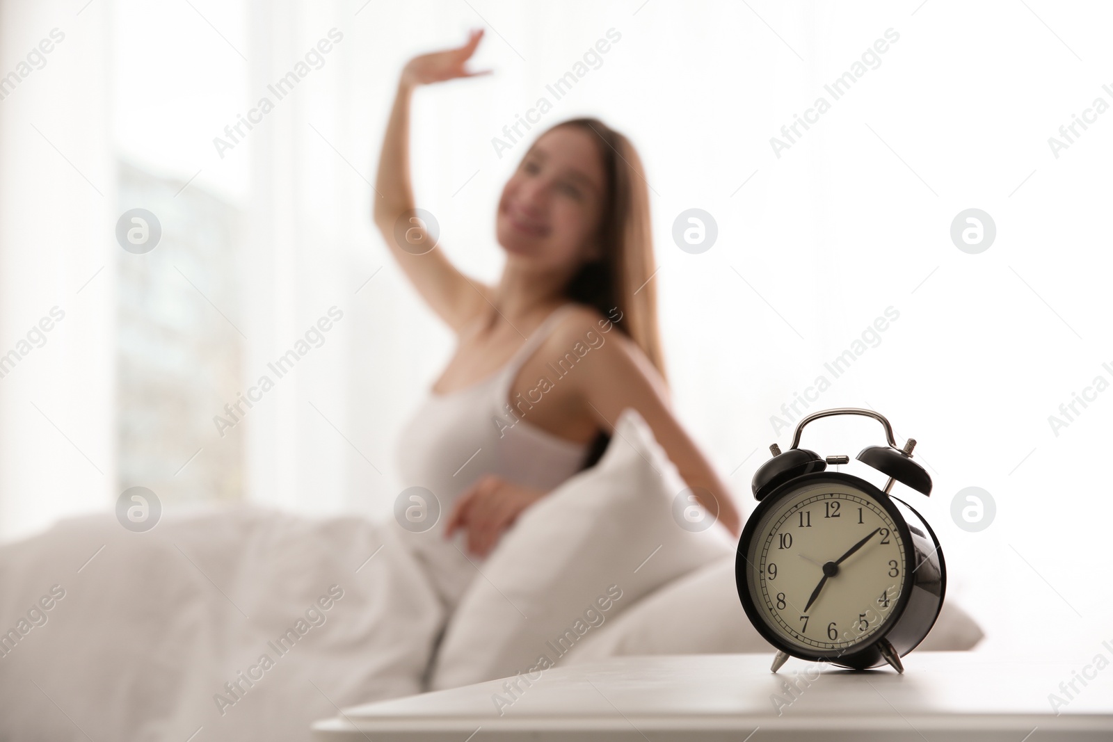 Photo of Young woman stretching at home in morning, focus on alarm clock