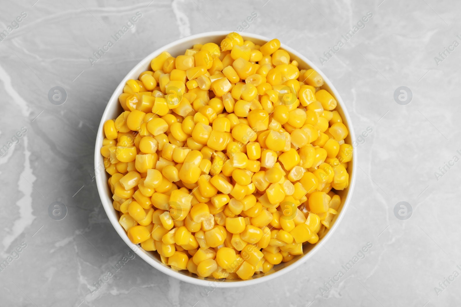 Photo of Delicious canned corn in bowl on marble table, top view