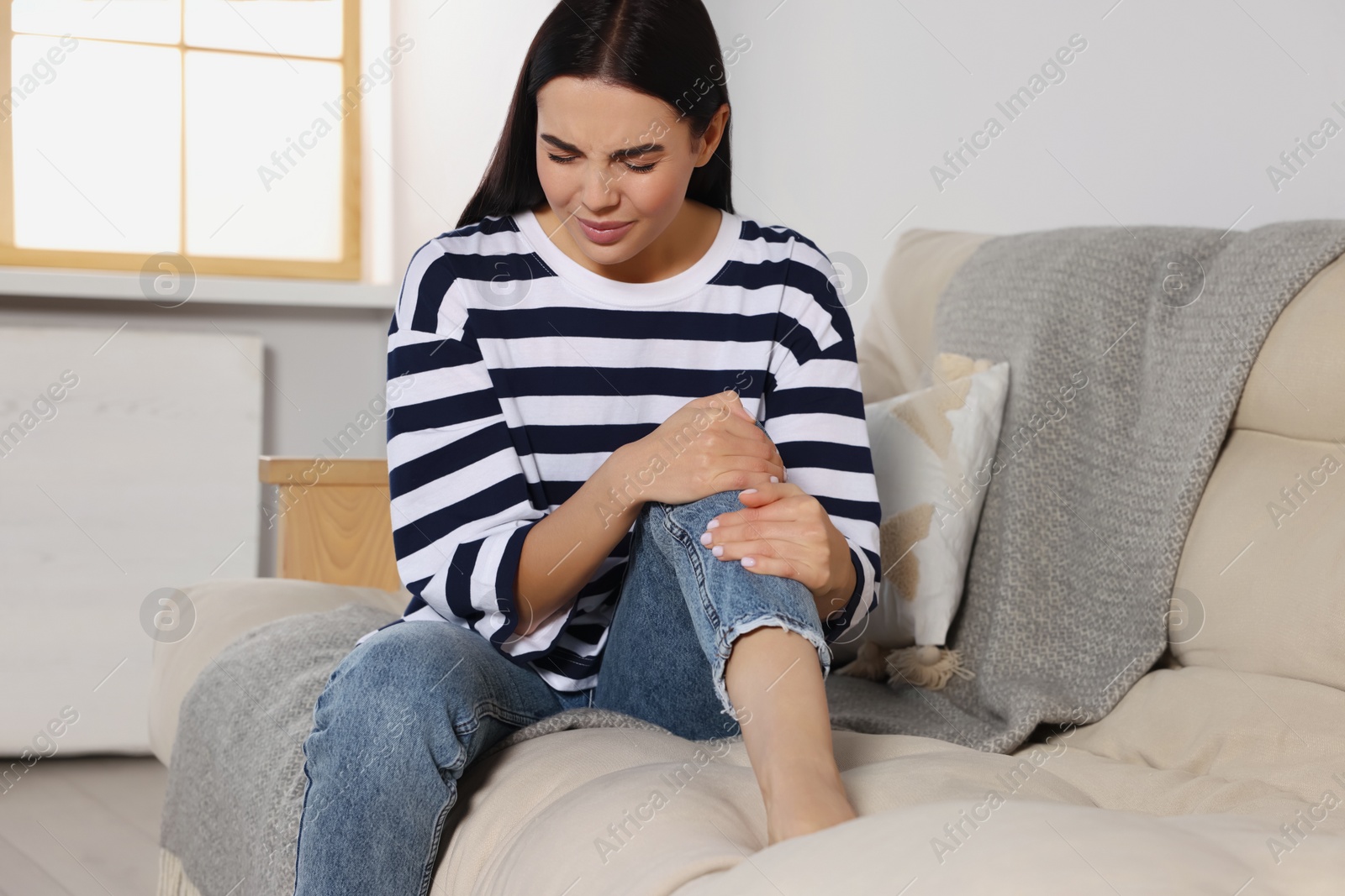 Photo of Woman suffering from knee pain on sofa at home