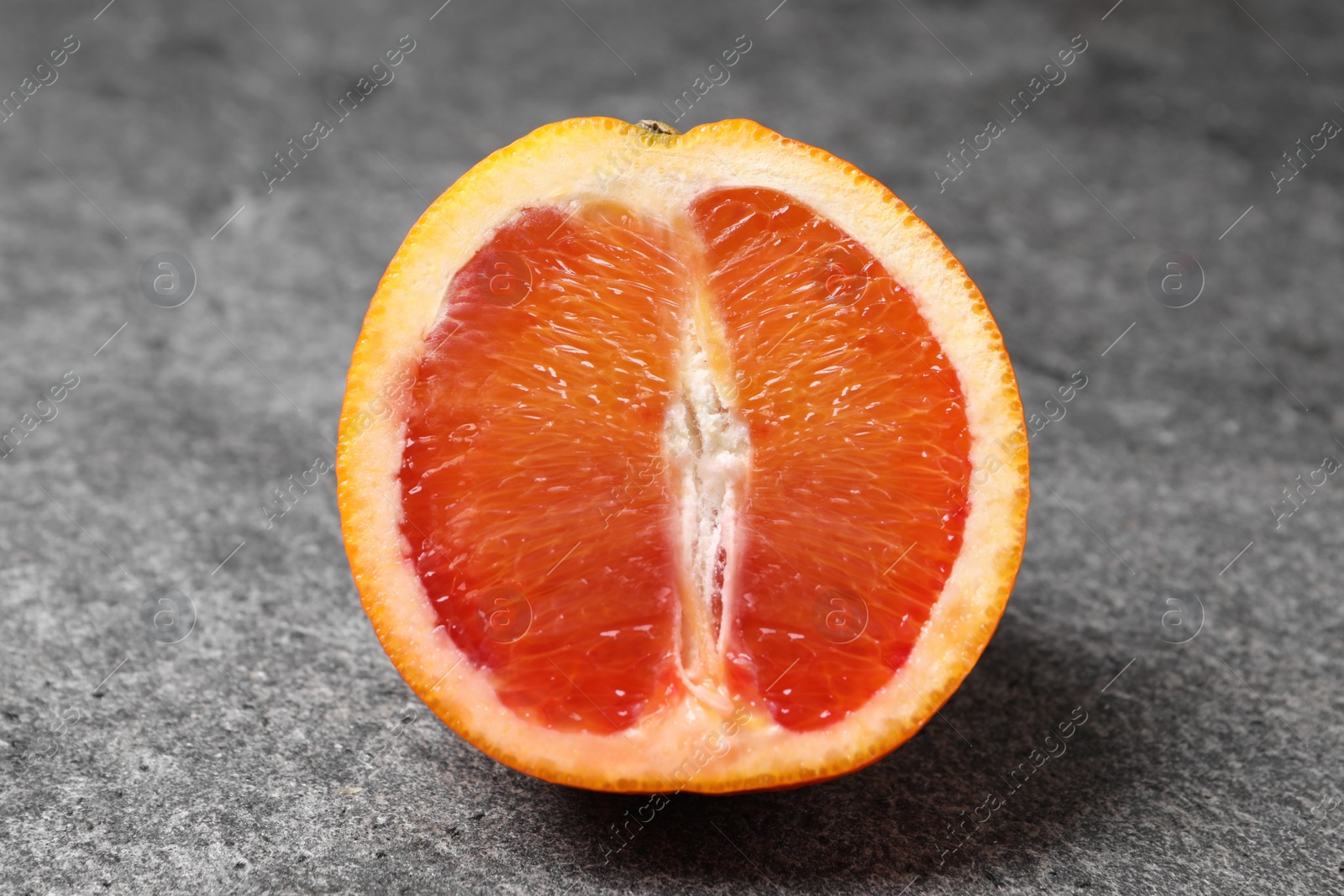 Photo of Half of ripe red orange on grey table, closeup