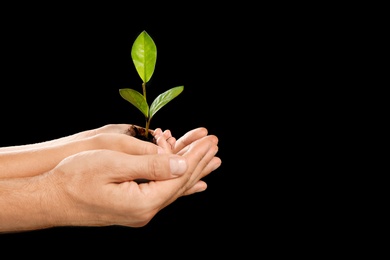 Photo of Man and his child holding soil with green plant in hands on black background. Family concept