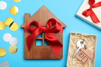 Photo of Wooden house model with red bow and key on light blue background, flat lay. Housewarming party