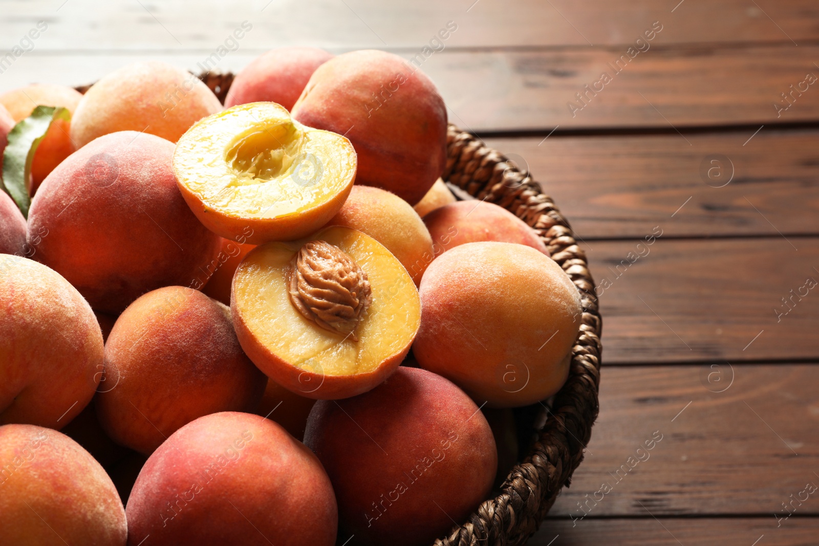 Photo of Wicker basket with fresh sweet peaches on wooden table, closeup