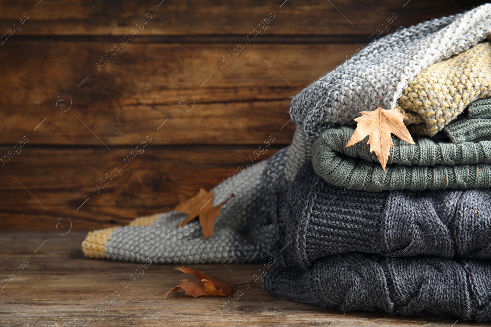 Photo of Stack of knitted plaids with dry leaves on wooden table, closeup