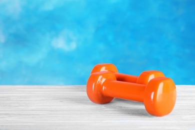 Photo of Stylish dumbbells on table against color background, space for text. Fitness equipment