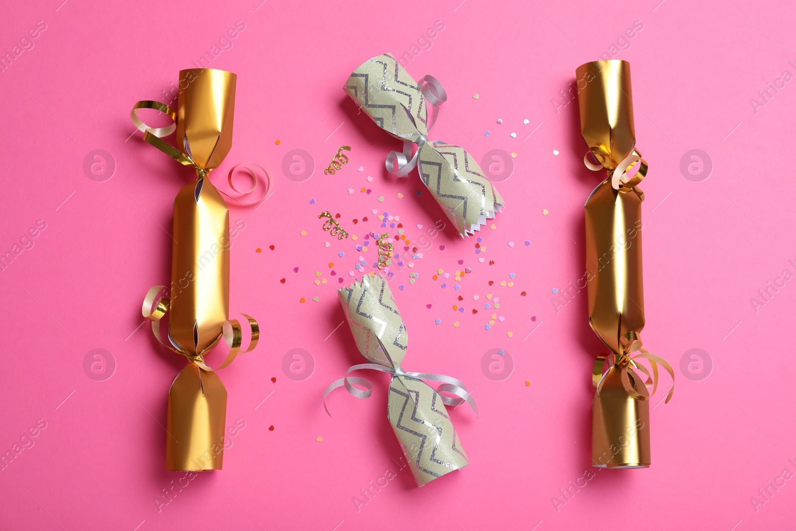 Photo of Open and closed Christmas crackers with shiny confetti on pink background, flat lay