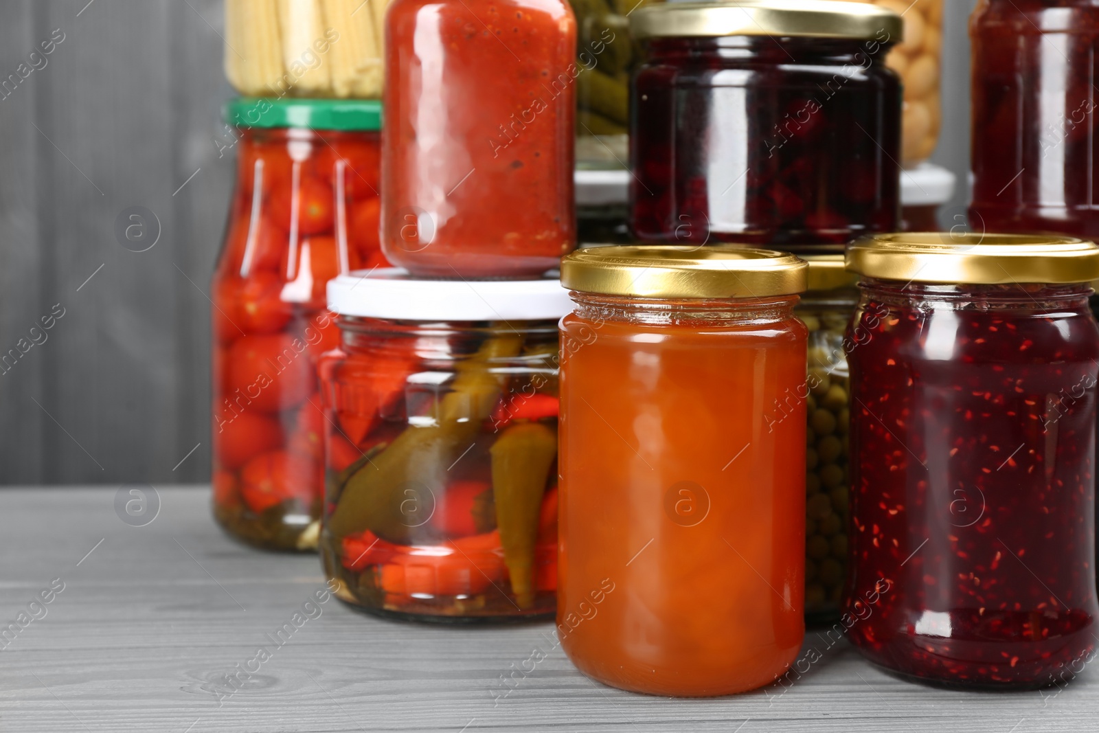 Photo of Glass jars with different pickled foods on grey wooden background, closeup