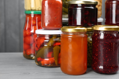 Glass jars with different pickled foods on grey wooden background, closeup