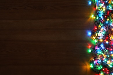 Photo of Colorful Christmas lights on wooden table, top view. Space for text