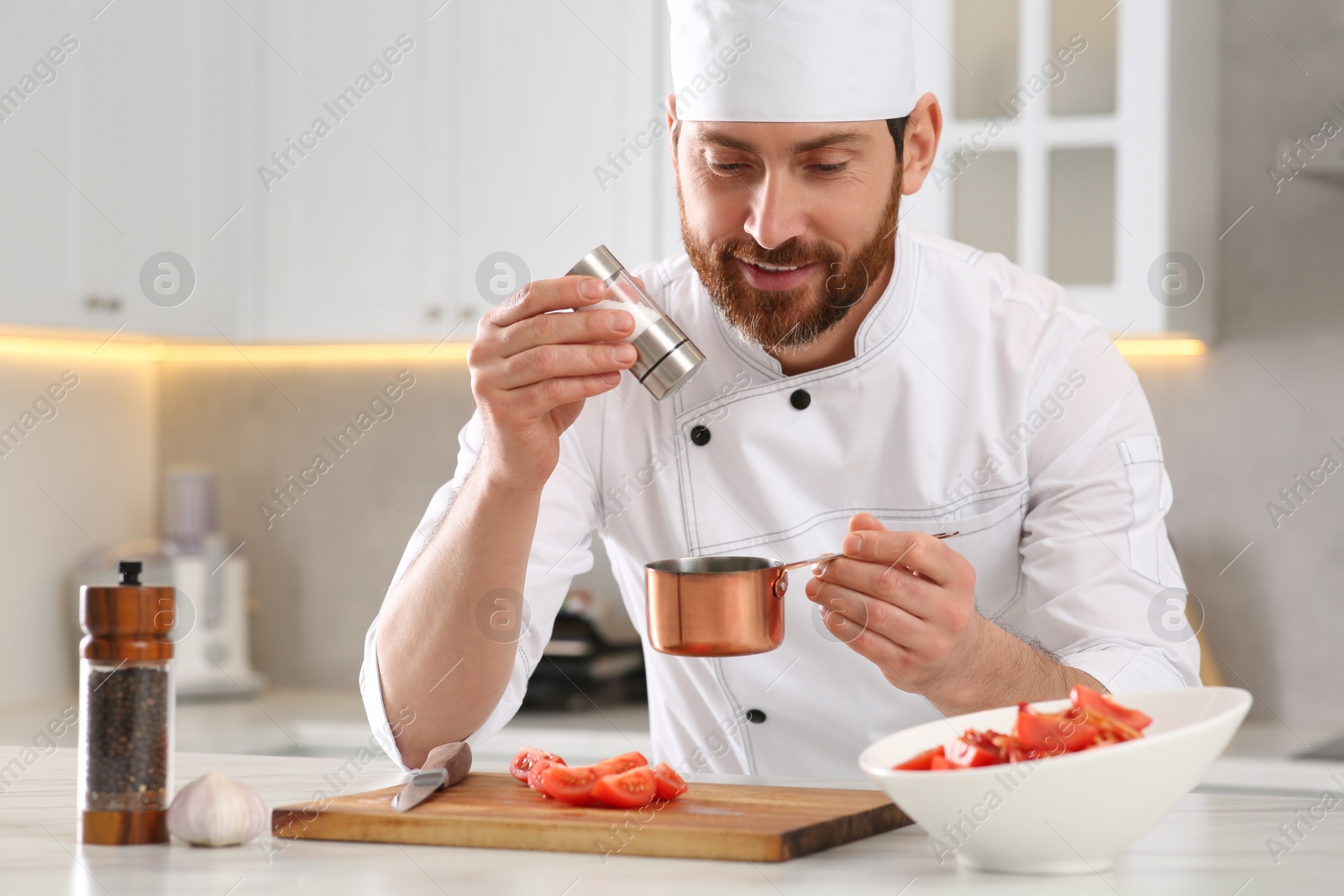 Photo of Professional chef adding salt into scoop at marble table in kitchen