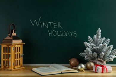 Photo of Text Winter Holidays on chalkboard near wooden table with Christmas decor and book