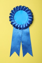 Photo of Blue award ribbon on yellow background, top view
