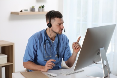 Photo of Doctor with headset consulting patient online at desk in clinic. Health service hotline