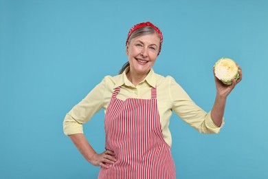 Happy housewife with half of cabbage on light blue background