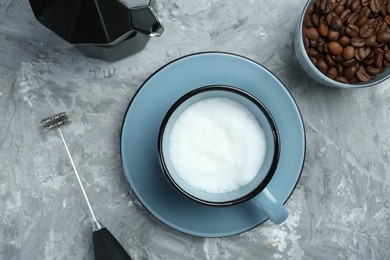 Photo of Mini mixer (milk frother), whipped milk in cup, coffee beans and moka pot on grey textured table, flat lay