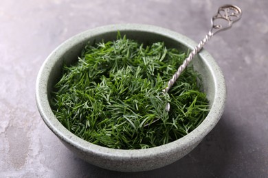 Photo of Fresh cut dill and spoon in bowl on grey textured table, closeup