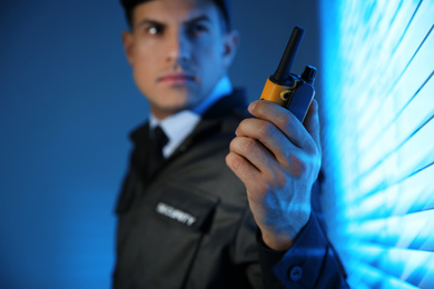 Professional security guard with portable radio set near window in dark room, focus on hand
