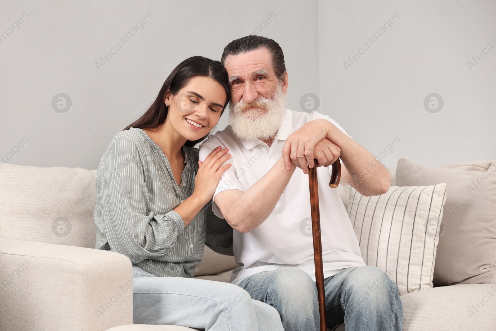 Photo of Senior man with walking cane and young woman on sofa indoors