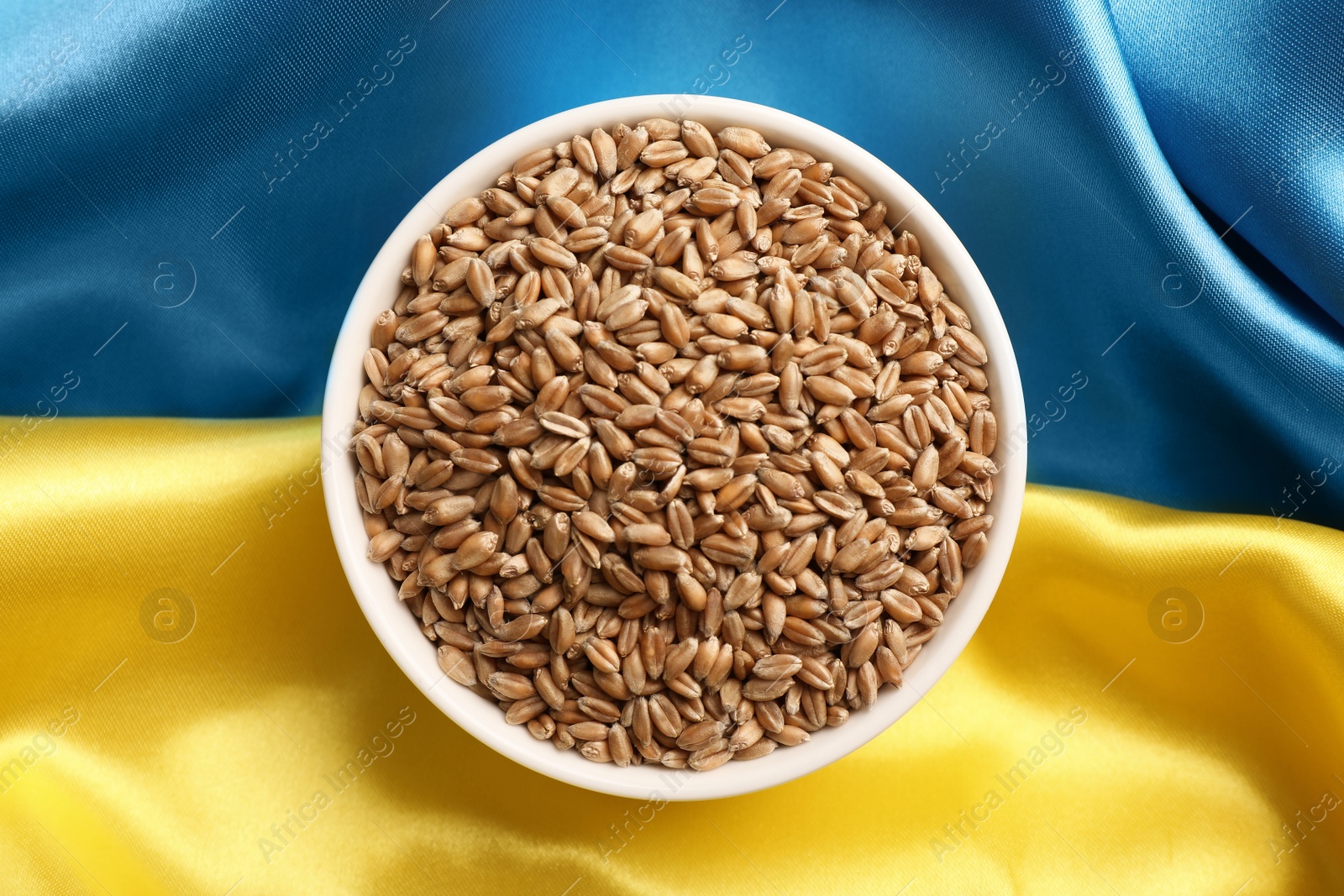 Photo of Bowl of wheat grains on Ukrainian flag, top view