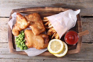 Photo of Tasty fish, chips, sauce and peas on wooden table, top view