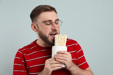 Young man eating delicious shawarma on grey background