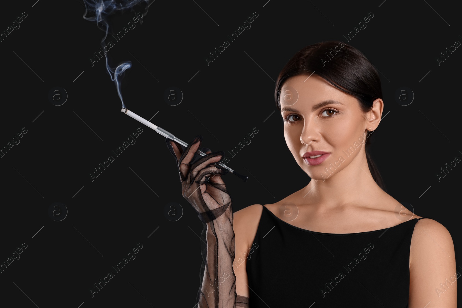 Photo of Woman using long cigarette holder for smoking on black background, space for text