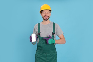 Photo of Professional repairman in uniform with phone on light blue background