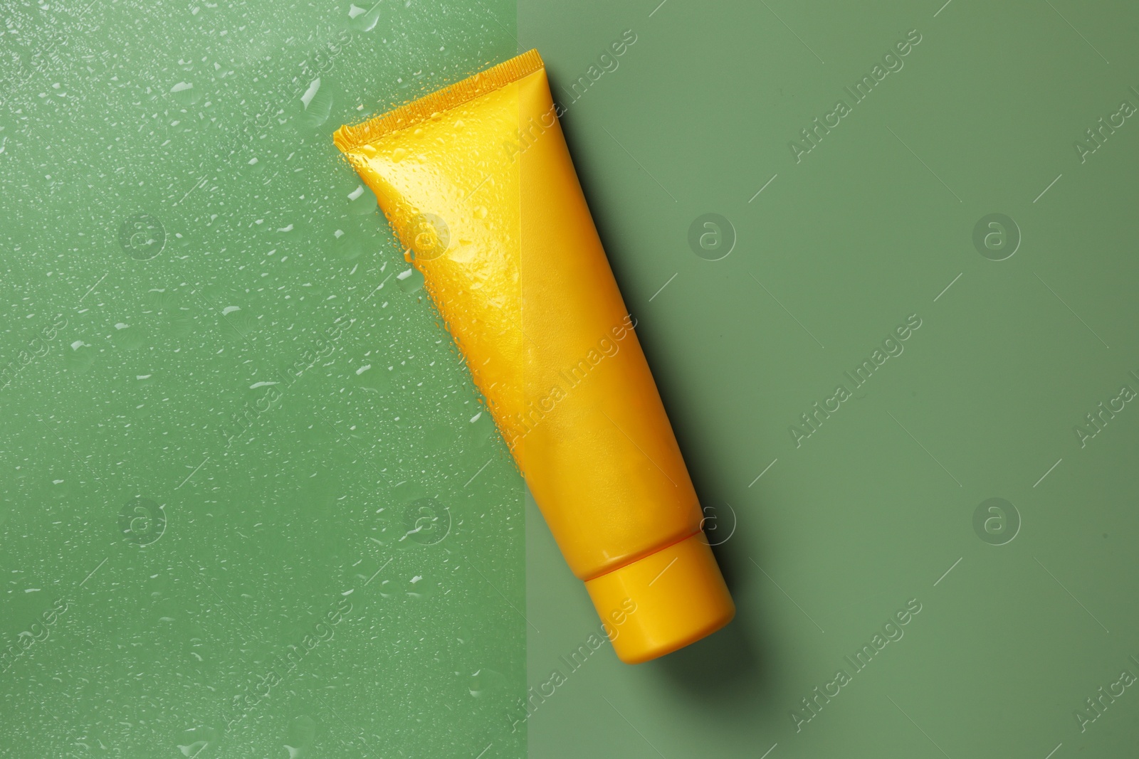 Photo of Tube with moisturizing cream on wet green surface, top view