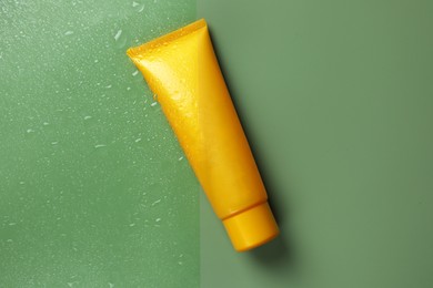 Photo of Tube with moisturizing cream on wet green surface, top view