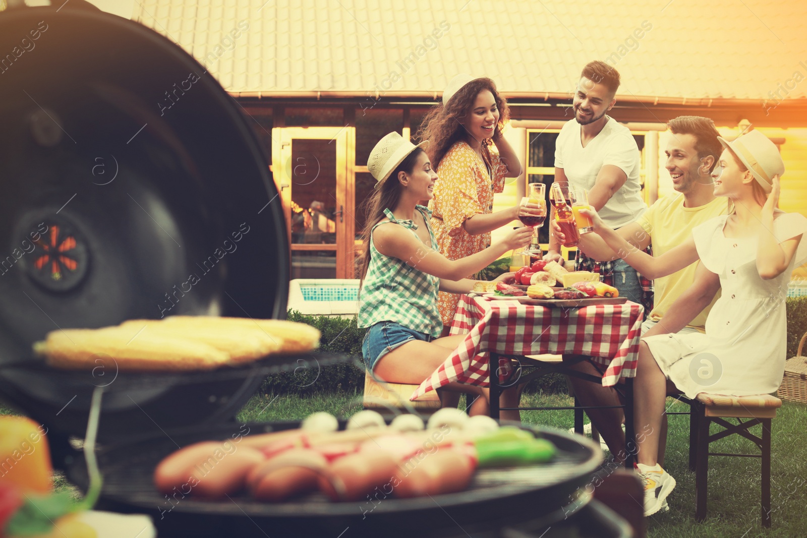 Image of Group of friends at barbecue party outdoors. Blurred view of grill with sausages and vegetables