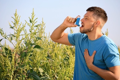 Photo of Man with inhaler suffering from ragweed allergy outdoors on sunny day