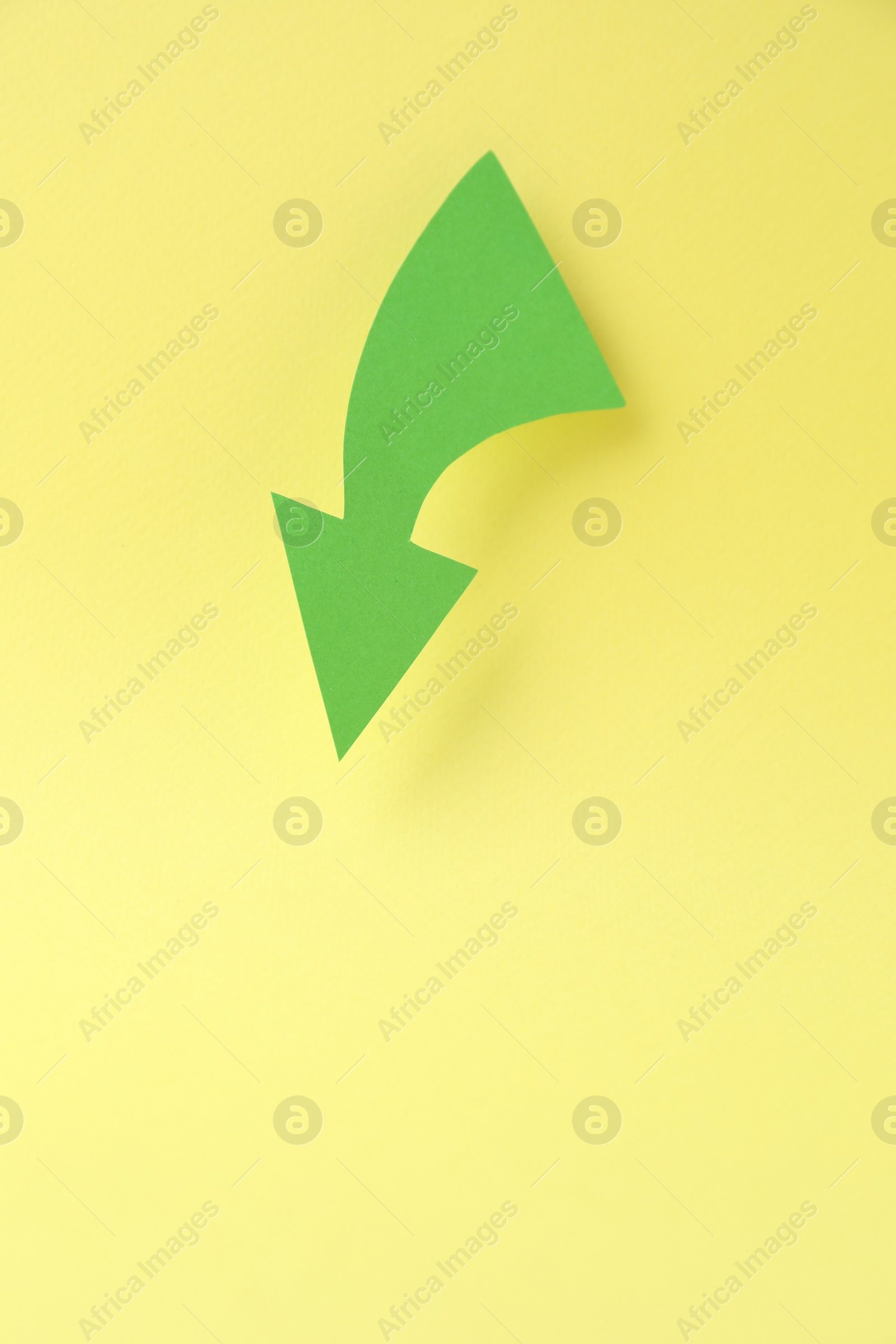 Photo of Curved green paper arrow on yellow background, top view. Space for text