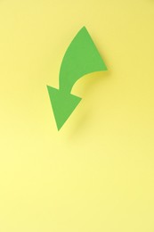 Curved green paper arrow on yellow background, top view. Space for text