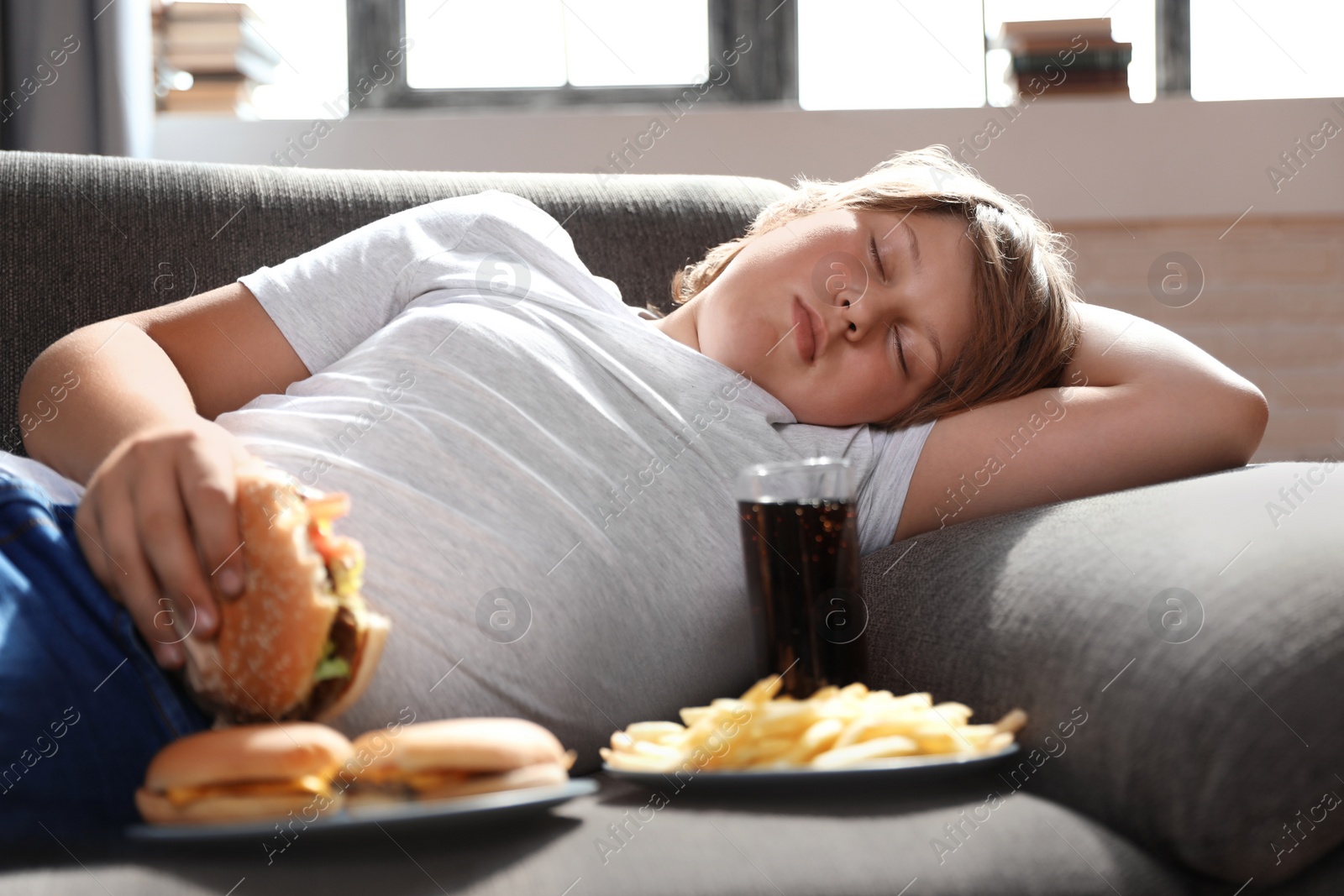 Photo of Overweight boy sleeping on sofa surrounded by fast food