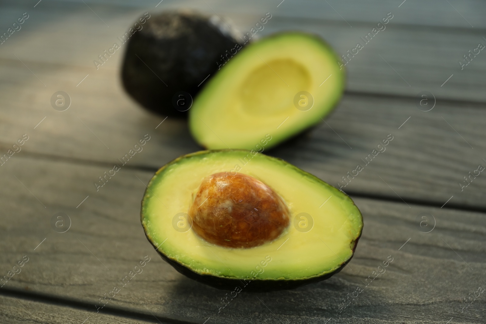 Photo of Half and whole fresh avocados on wooden table, closeup