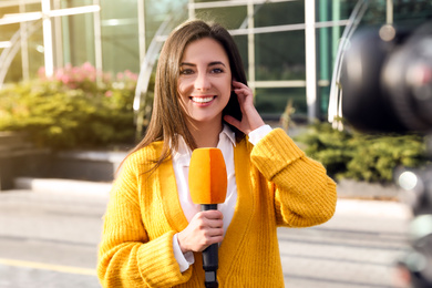 Young female journalist with microphone working on city street