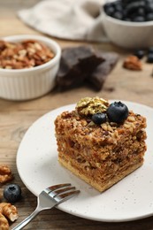 Piece of delicious layered honey cake with blueberries and nuts served on wooden table, closeup
