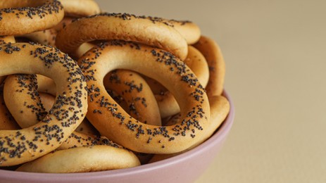 Photo of Bowl with delicious ring shaped Sushki (dry bagels) on beige background, closeup. Space for text