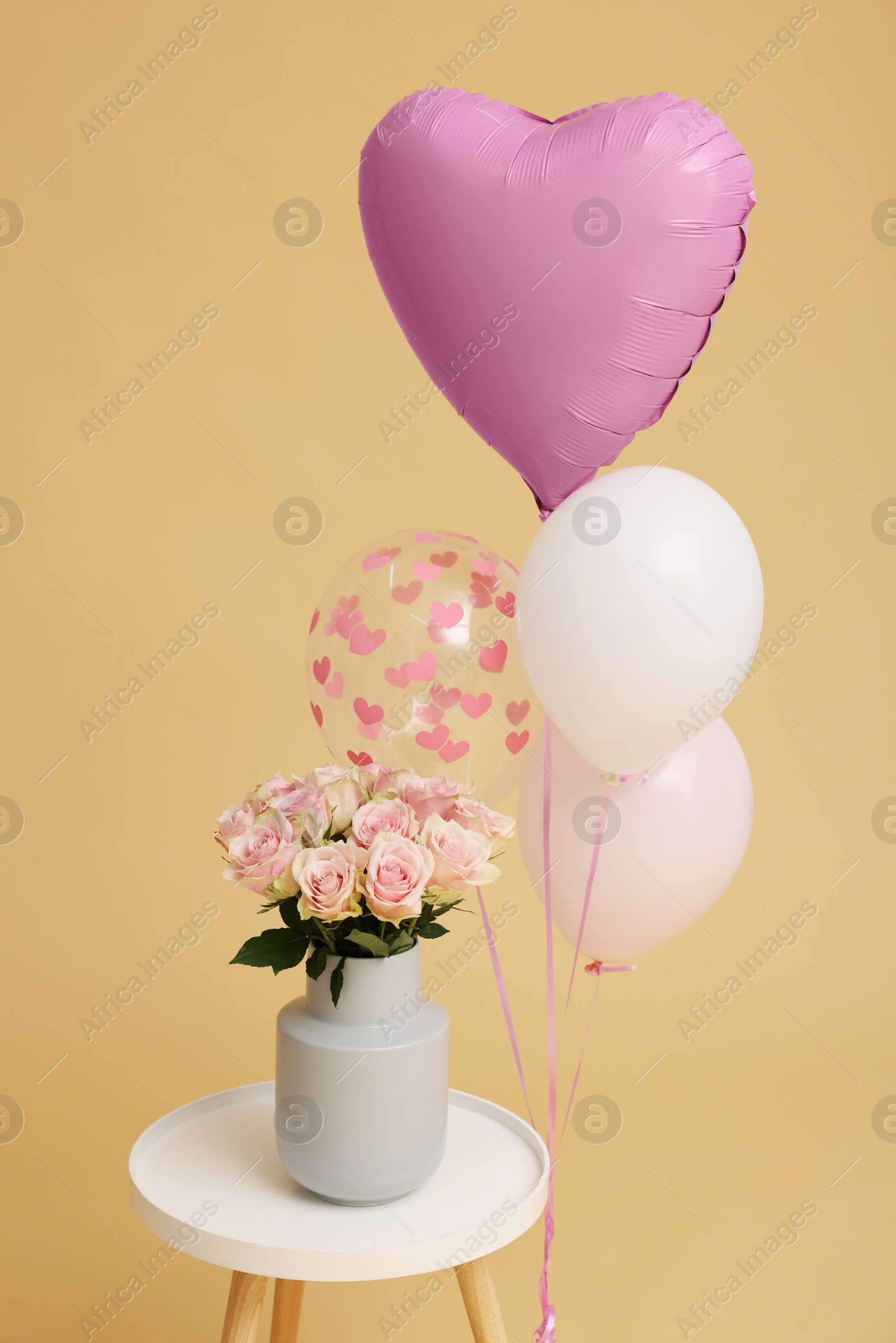 Photo of Bunch of different shaped balloons and beautiful rose flowers on coffee table for birthday party against beige background