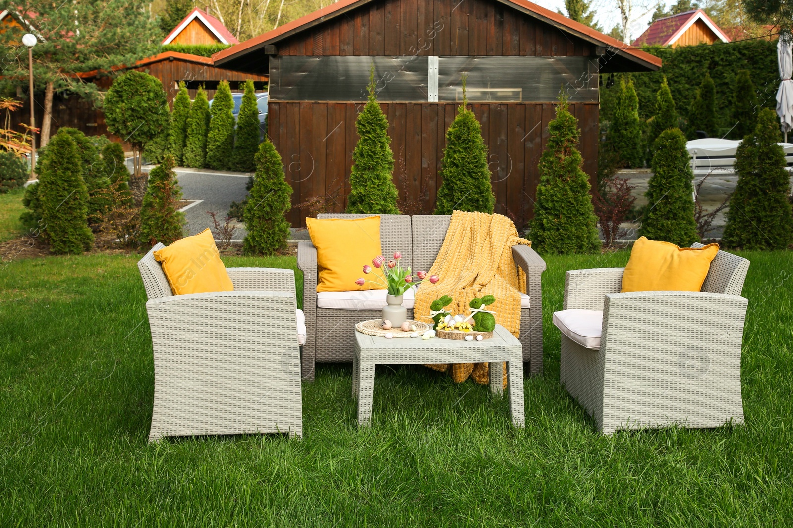 Photo of Easter decorations. Bouquet of tulips in vase, bunny figures and decorated eggs on table in backyard